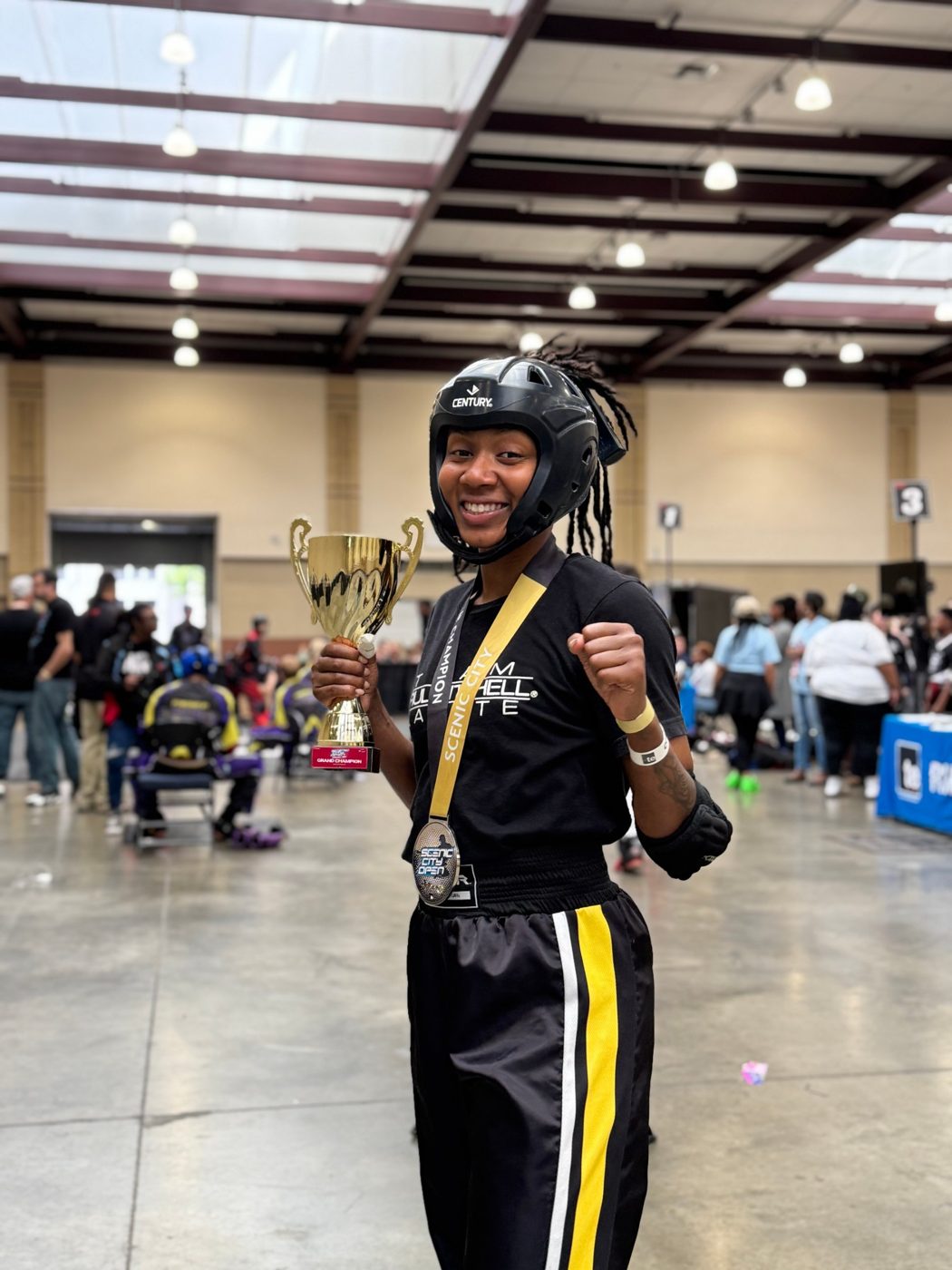 Ki'Tana Everett holding a grand champion trophy at the Scenic City Open, in Century headgear and a Team Paul Mitchell shirt